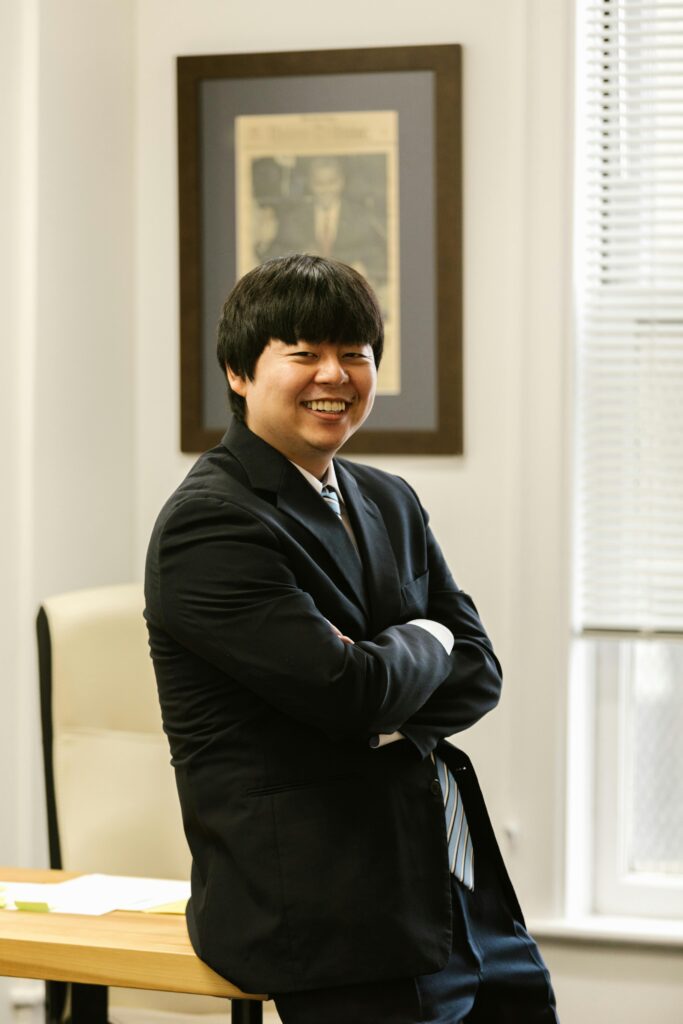 Smiling businessman in a black suit confidently standing in a modern office space.